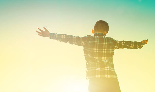 istock Boy embrace the sun as it sets on the sky 471883772