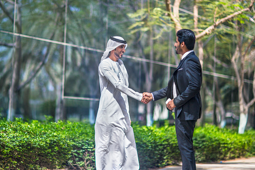 Middle Eastern businessmen shaking hands on an agreement ,one is wearing the typical dishdasha and the other a suit.