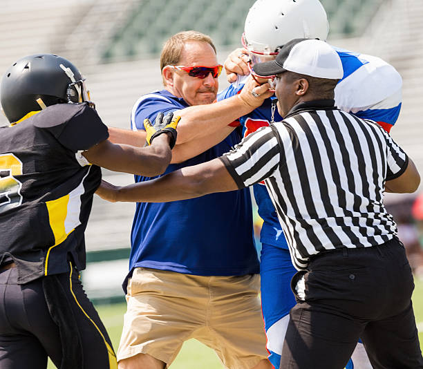 Coach and referee breaking up football players during game