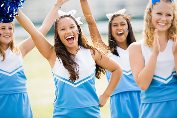 Excited high school cheerleaders performing at football game Excited high school cheerleaders performing at football game cheerleader photos stock pictures, royalty-free photos & images