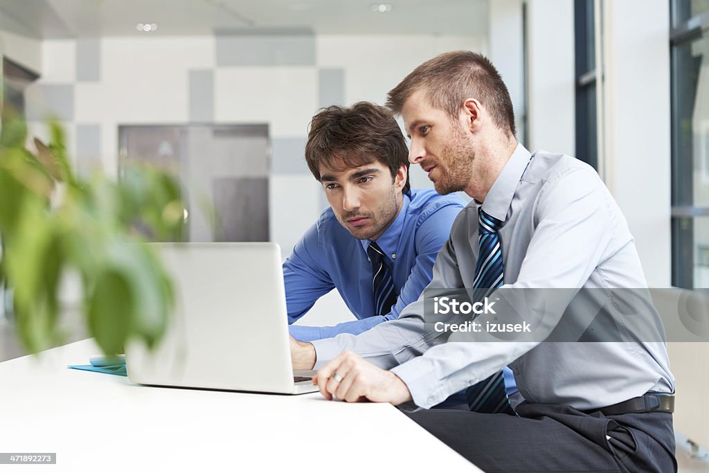 Business people working together Two businessmen sitting in an office and working together on the laptop.  Adult Stock Photo