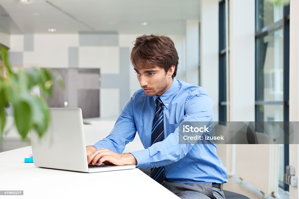 Businessman using laptop Businessman sitting in an office and working on the laptop.  Adult Stock Photo