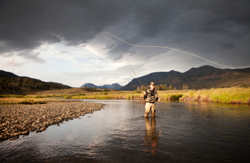 Man fly fishing on a western U.S. stream with storm clouds in the background.