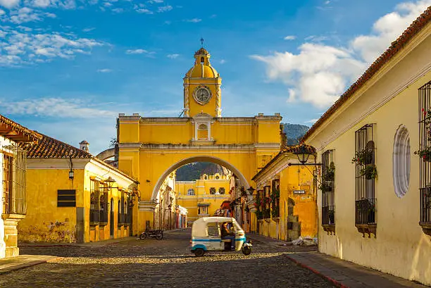 a tuk-tuk taxi passes in from of The Arch of Santa Catalina in Antigua, Guatemala.