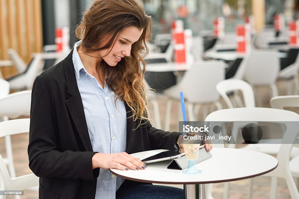 Woman looking at her tablet computer siting in a bar Portrait of a woman looking at her tablet computer, smiling and sitting in a coffee shop Cafe Stock Photo