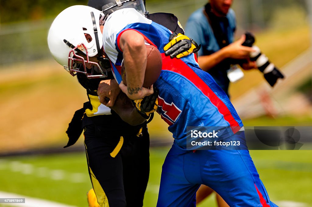 Sports:  Football running back carries the ball. Football players on field during game.  Running back carries the ball.  Defender tackles the player.  Sports photographer in background. Sports Photographer Stock Photo