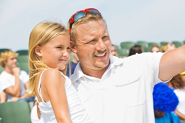 père tenant la jeune fille lors d'événements sportifs dans stadium - sport parent bleachers family photos et images de collection