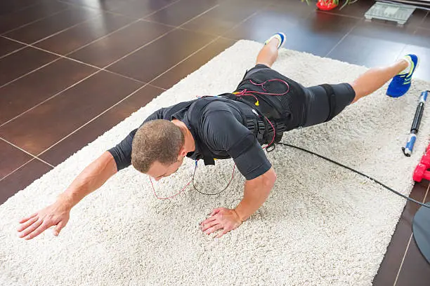 Rear view of a man who is doing press ups while receiving electric impulses from a hi tech stimulator