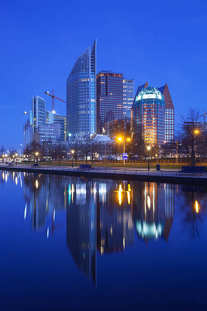 Vertical version of the skyline of The Hague in the Netherlands. The photo is taken in the blue hour during twilight. The buildings you see are almost all government buildings. The skyline is reflected in the water of a pond.