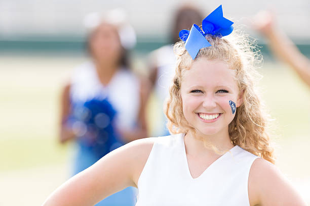 istock Adorable high school cheerleader smiling while cheering at game 471907379