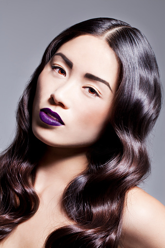 Beautiful Asian woman with glamorous hair and make-up, looking elegant and feminine. Purple lips and curly hair.