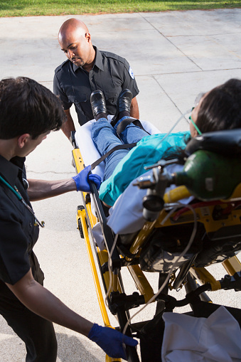 Multi-ethnic paramedics loading woman lying on stretcher onto ambulance.