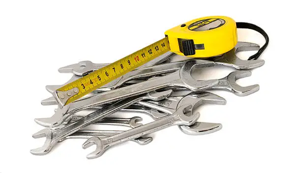 A pile of spanners, wrenches, keys and roulette, tape, tape-measure, tape-line, reel on a white background