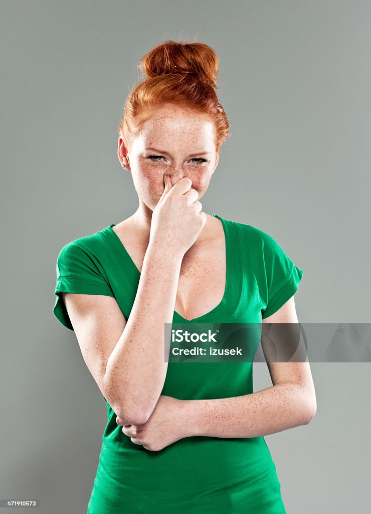 Woman pinches nose Portrait of disgusted teenage girl pinches her nose and looking at the camera. Studio shot, gray background. Unpleasant Smell Stock Photo