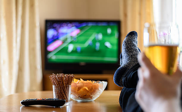 TV watching (football match) with feet on table and snacks Television, TV watching (football match) with feet on table and huge amounts of snacks - stock photo remote control on table stock pictures, royalty-free photos & images