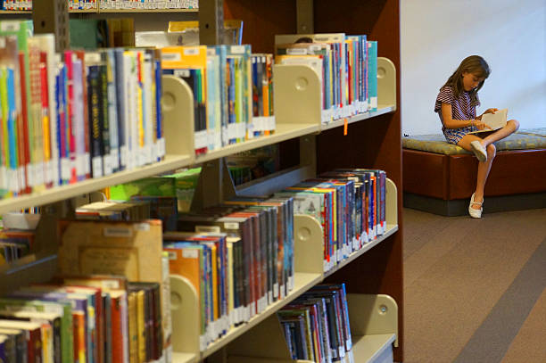 istock Little girl reading a book in school library 471910757