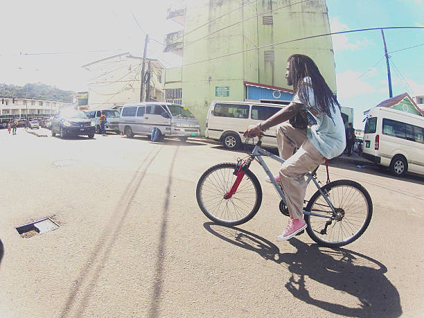 Castries, St Lucia - October 15, 2013: A ratasfarian man in pink shoes rides a bike on lower Darling road Castries with Omnibuses lined up waiting for passengers in background. Shot on GoPro Hero 2 Camera.