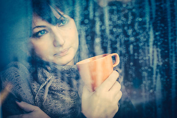 istock Woman with hot drink looking through a window 471913349