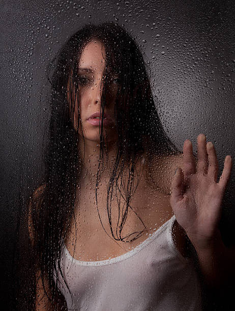 A beautiful girl in a white t-shirt, on a black background behind the wet glass.