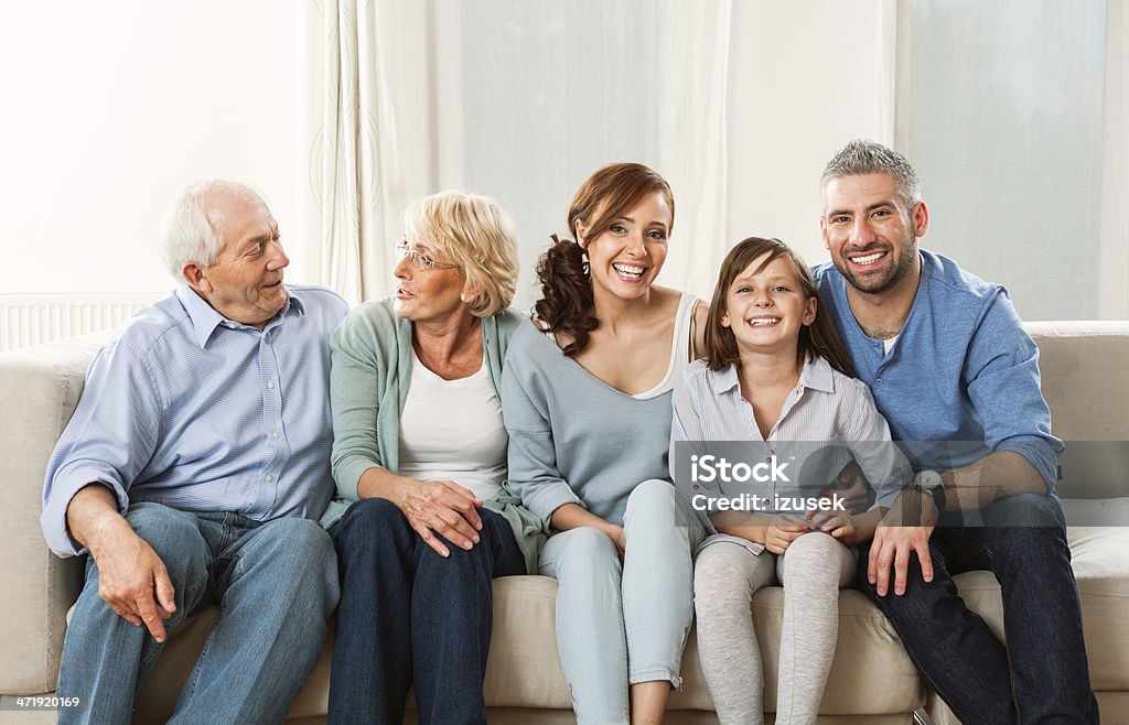 Three generation family Grandparents, patents and cute girl sitting on sofa at home and laughing. Crowded Stock Photo