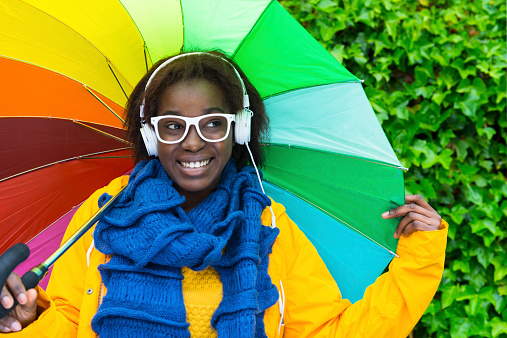 Cheerful woman enjoying music and carrying a colorful umbrella in a rainy day.