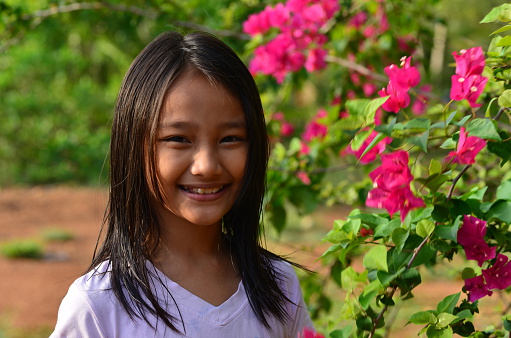 Image of a pretty nine year girl standing next to flowers at her family home garden, where she helps her family in the daily chores of running holiday bungalows for tourists who visit the island. Her name 'Ice' pronounced 'Eye\