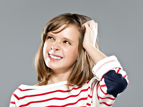 Portrait of cute girl wearing striped blouse looking away with hand in hair. Studio shot.