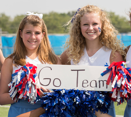 High school cheerleaders with pom-poms and a 'go team' sign.  Posing and smiling for camera.