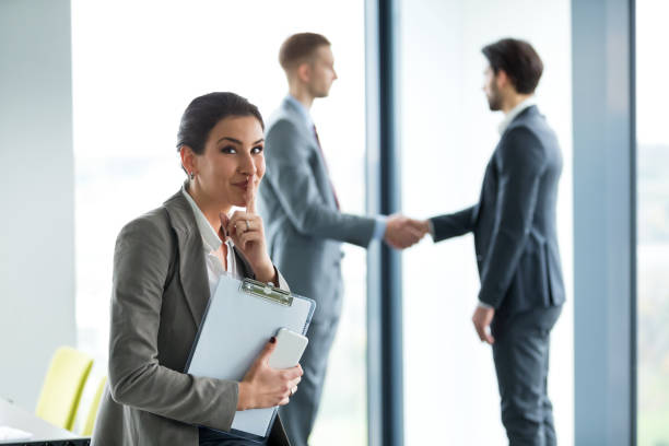 istock Businesswoman shushes with a smile as two men shake hands  471929600