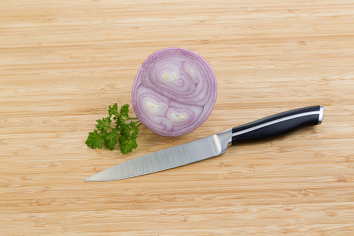 Horizontal photo of sliced purple onion and small piece of parsley with single knife lying on natural bamboo cutting board