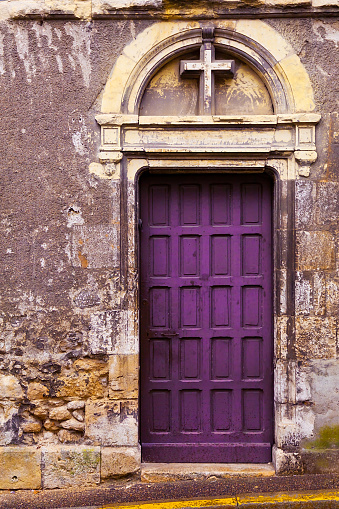 A royalty free DSLR photo of a slightly asymmetrical composition inviting entry through a royal purple door crowned by a cross in an archway--Christian religious symbols.