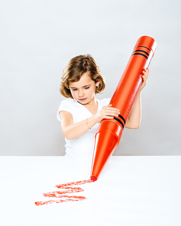 Little girl drawing with oversized crayon.