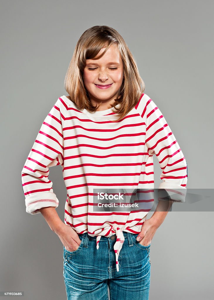 Playful girl Portrait of cute girl wearing striped blouse smiling with hands in pockets. Studio shot, grey background. 10-11 Years Stock Photo
