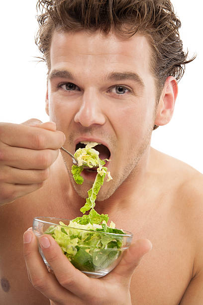 Man Eating Salad Young fit man eating raw green healthy vegetarian salad in glass bowl. eating body building muscular build vegetable stock pictures, royalty-free photos & images