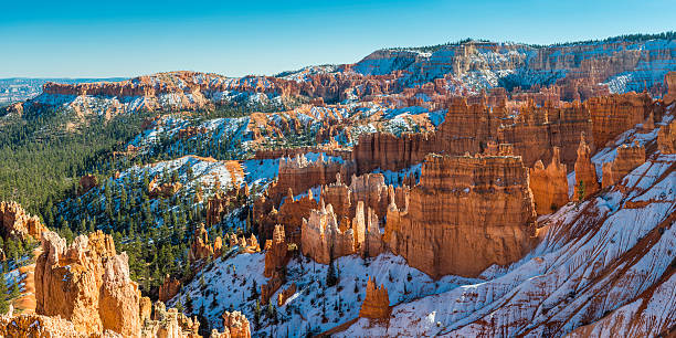 Bryce Canyon National Park colorful hoodoos snow panorama Utah USA The golden sandstone hoodoo pinnacles of Bryce Canyon National Park glowing in the bright winter light amongst the snow covered forests of the Paunsaugunt Plateua, Utah, USA. ProPhoto RGB profile for maximum color fidelity and gamut. sunrise point stock pictures, royalty-free photos & images