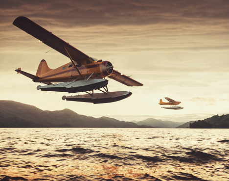Two float planes at low altitude in sunset light over an Alaskan inlet.  Shot at high iso with light grain.