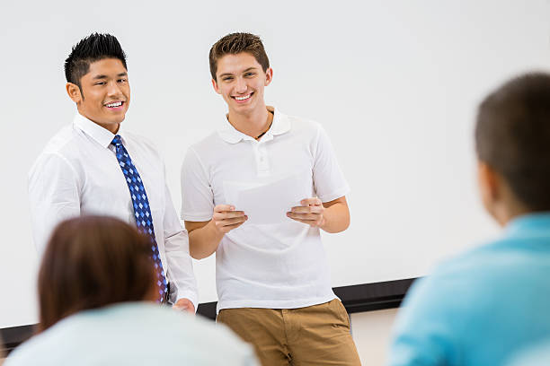 istock Teacher introducing student as he gives report to class 471948195