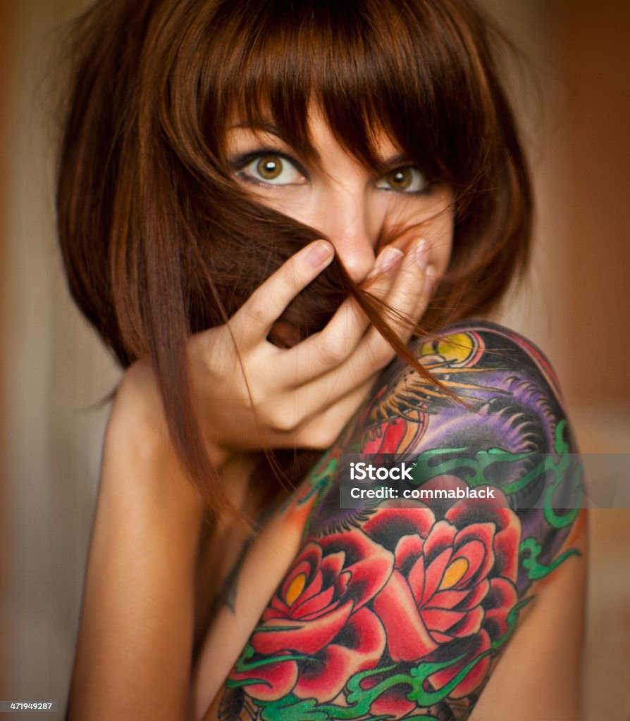 Tattooed girl European girl  with tattoo on her shoulder covering her mouth with arm looking at camera Tattoo Stock Photo