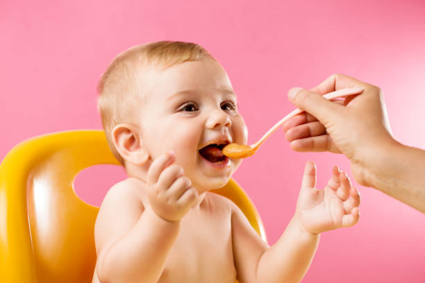 Feeding cheerful baby on pink background Mother's hand feeding a laughing baby in front of a vivid pink background. baby spoon stock pictures, royalty-free photos & images