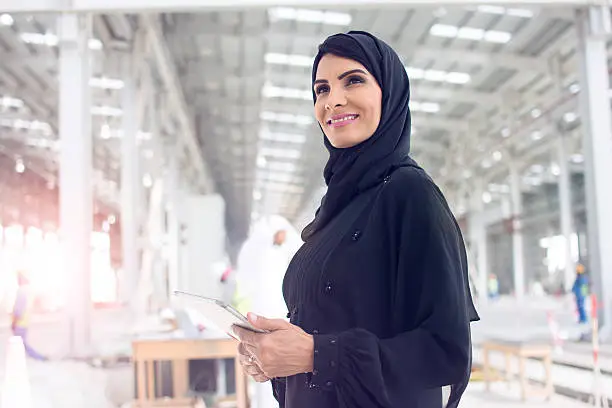 Confident Arab woman dressed in abaya looking forward while holding a digital tablet.