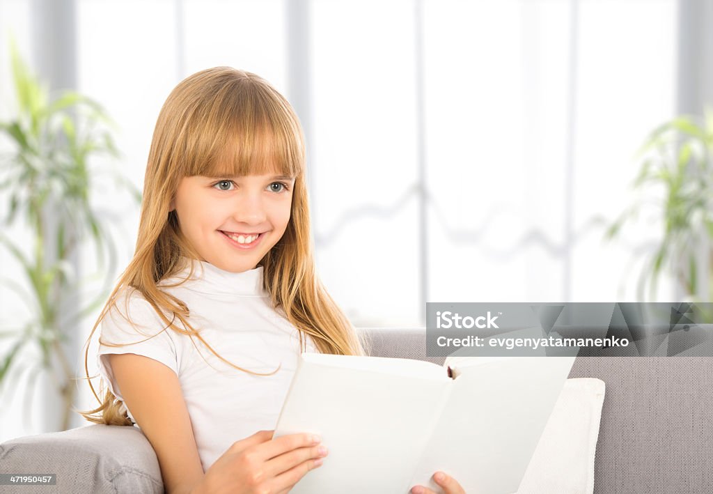 Criança feliz menina lendo um livro sentado no sofá - Foto de stock de Adolescente royalty-free