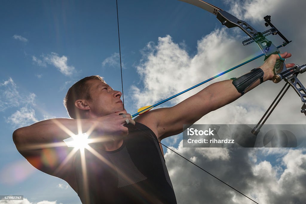 Man with bow and arrows Tough man with bow and arrows, close up with cloudy sky at background. Activity Stock Photo