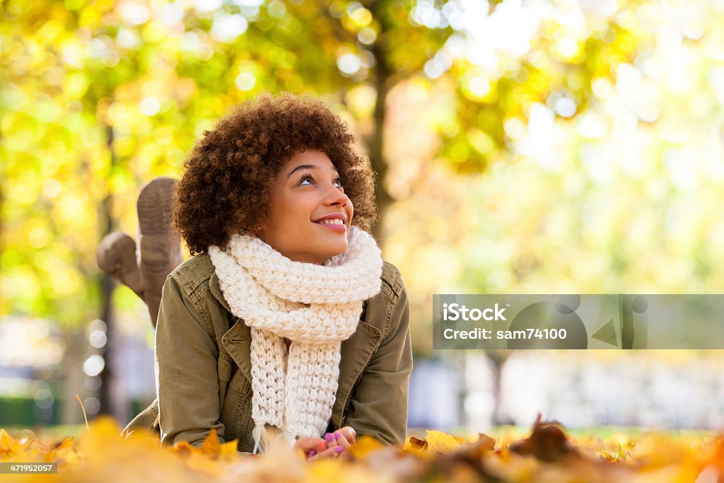 Young smiling African American woman lying on fall leaves Autumn outdoor portrait of beautiful African American young woman lying down - Black people Autumn Stock Photo