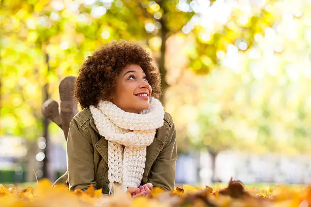 Photo of Young smiling African American woman lying on fall leaves