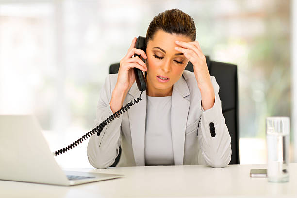 Stressed businesswoman taking a phone call at her desk stock photo