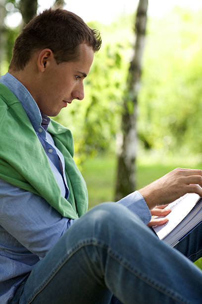 istock Young man reading book in park 471953962