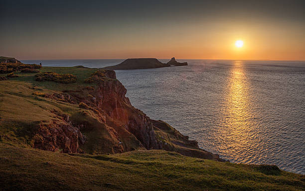 Sunset at Worms head rhossili bay Iconic piece of land jutting out from Rhossili bay on the Gower peninsular, south Wales. gower peninsular stock pictures, royalty-free photos & images