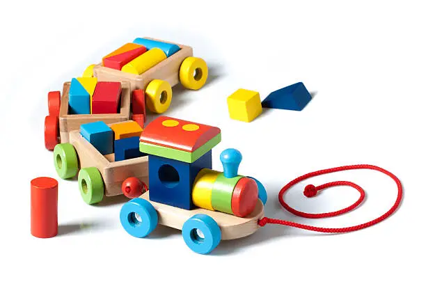 A wooden toy train carrying puzzle pieces as cargo,  painted in many colors, pulled by a red string. Isolated on white background.