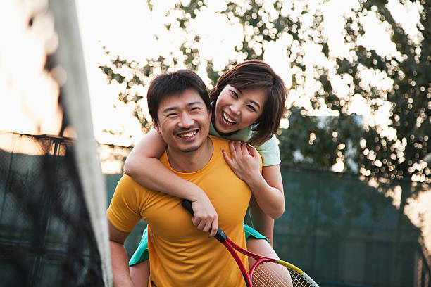 Boyfriend holding his girlfriend next to the tennis net Boyfriend holding his girlfriend next to the tennis net mid adult couple stock pictures, royalty-free photos & images