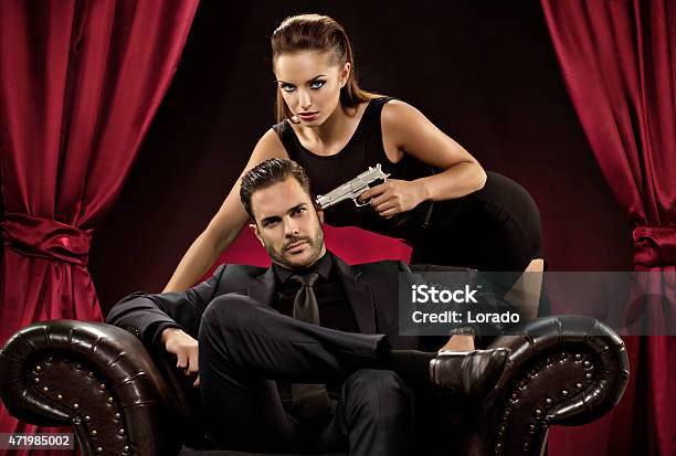 Woman Pointing Gun To Man Sitting On Chair Stock Photo - Download Image Now - Men, Women, Gangster